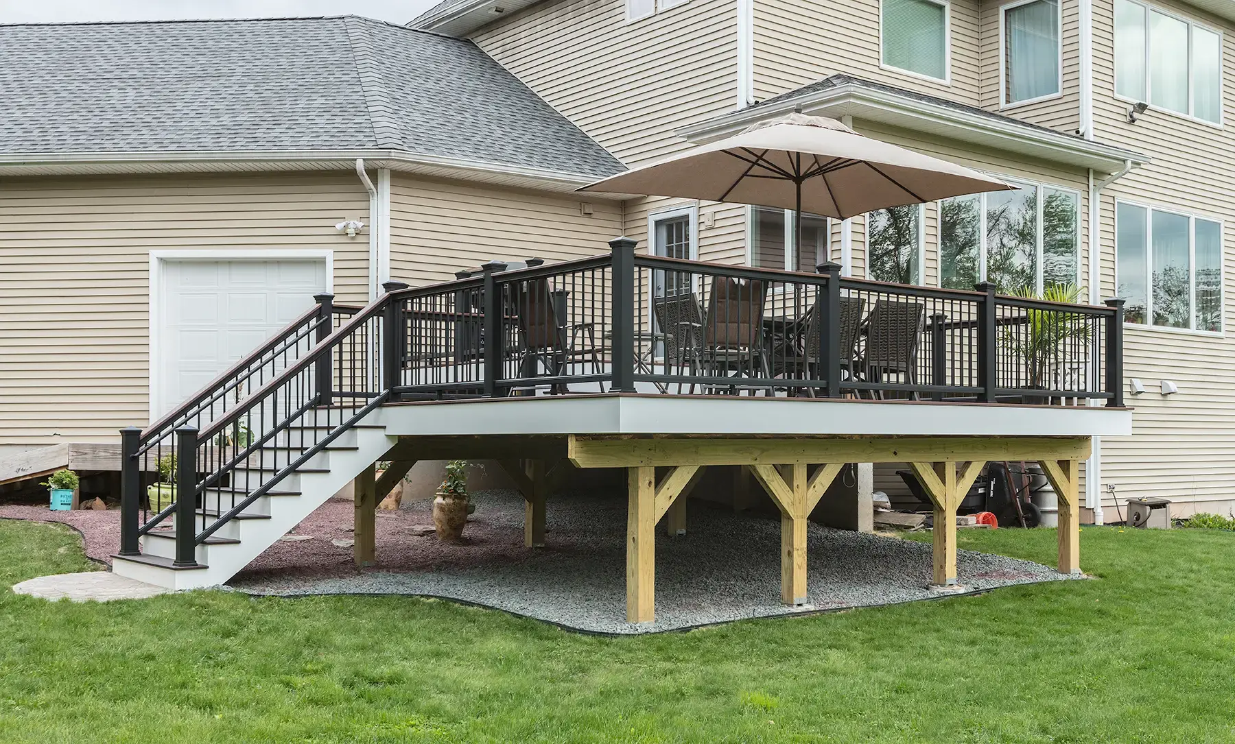 Elevated deck with black metal railing, shade umbrella and wide stairs over a gravel base