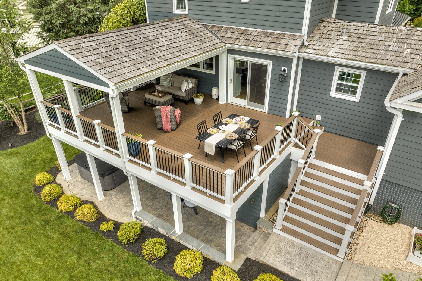 Two-story covered deck with a shingle roof, dining table, lounge seating and stairs down to a stone patio