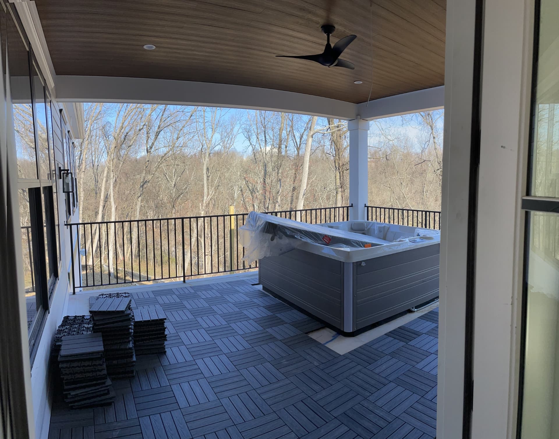 Covered deck with wood-look ceiling, ceiling fan, black railing and a hot tub