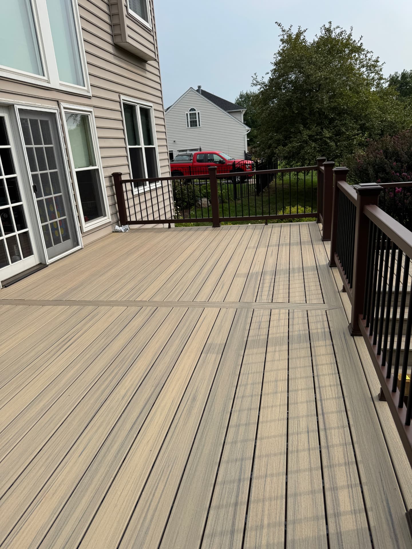 Tan composite deck with brown railing and black balusters behind a suburban home
